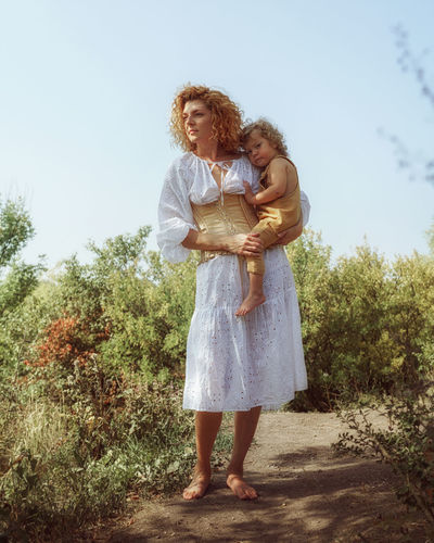 Full length of woman with a baby son  standing by tree against sky