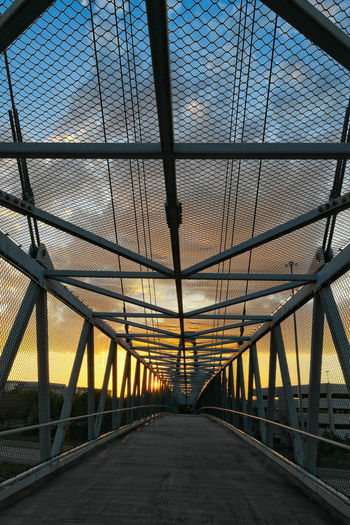 Footbridge over road against sky at sunset