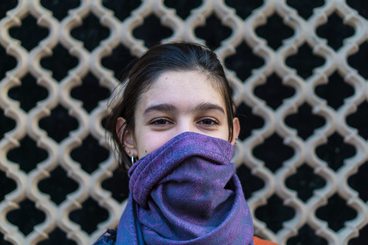 Portrait of woman covering face with scarf standing by wall