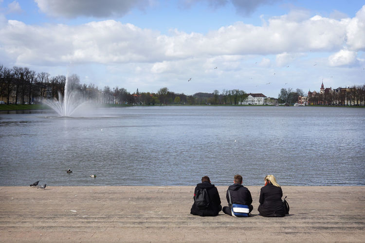 Rear view of three people sitting at lakeshore