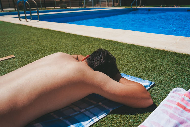 Shirtless man lying on grass by swimming pool