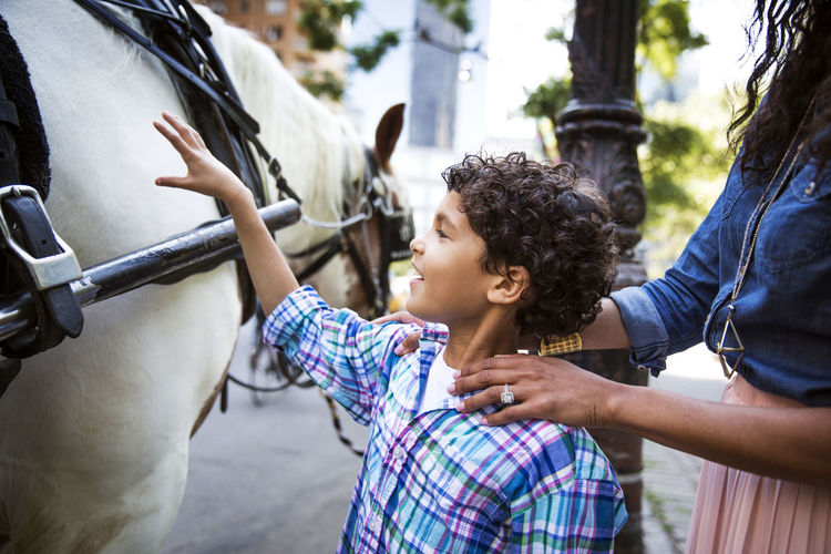 Boy touching horse while standing on footpath