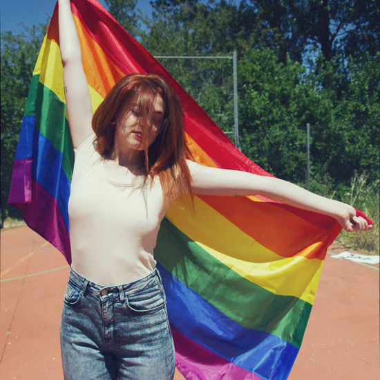 Young woman holding rainbow flag on sunny day