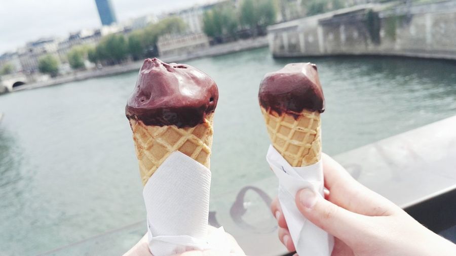 Cropped hand of woman holding ice cream cones against river