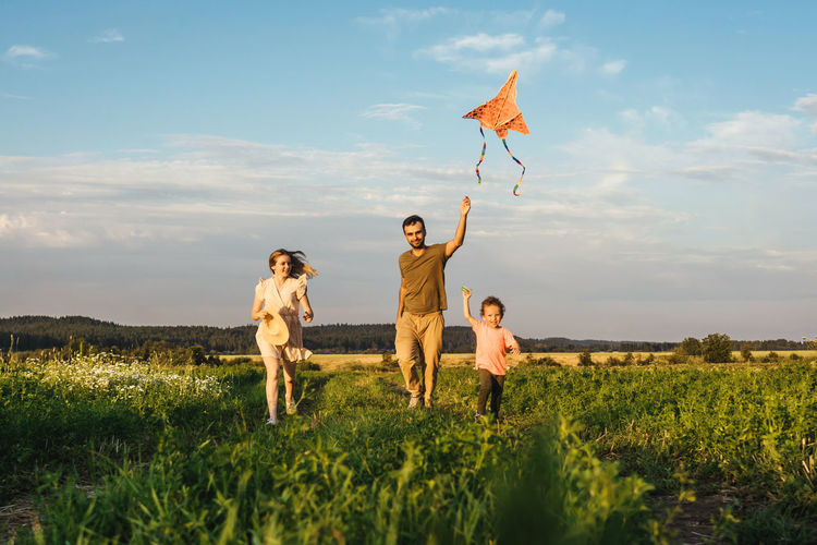 Family running on grassy land against sky