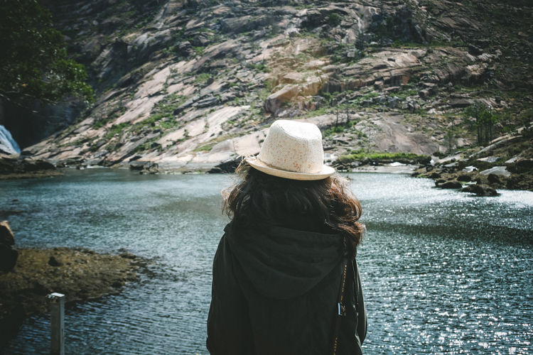 Rear view of woman wearing hat and jacket while looking at river by mountain