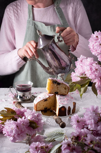 A woman pours tea from a silver teapot, background of pink sakura flowers,easter
