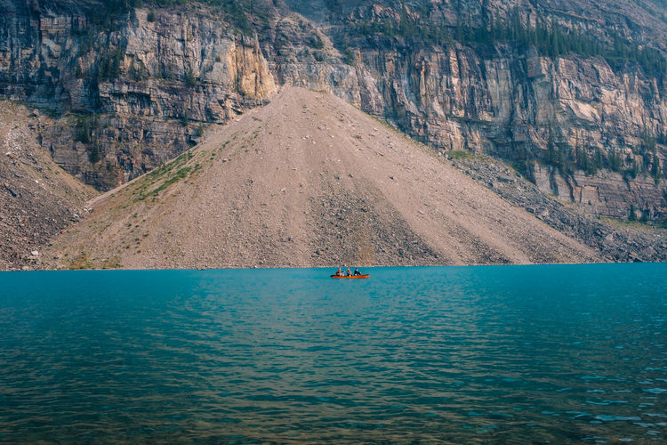People kayaking on sea against mountains