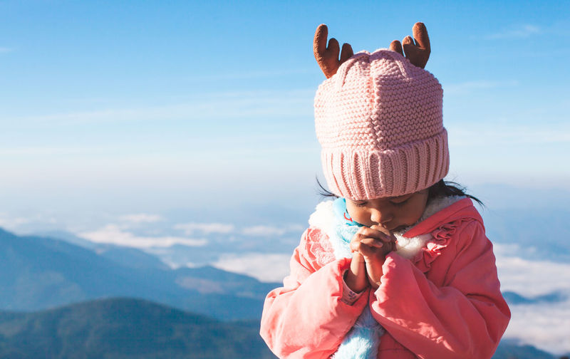 Cute girl praying against sky