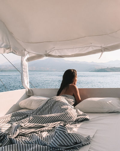 Shirtless woman lying on bed against sea