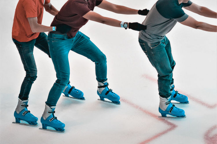 Low section of male friends ice-skating on rink