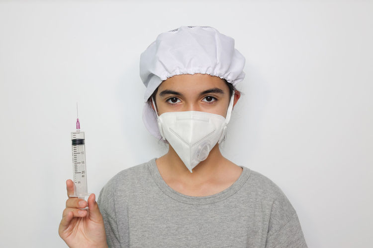 Portrait of doctor wearing mask holding syringe against white background