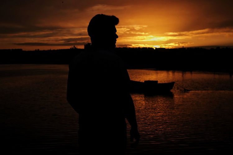 Silhouette man standing in lake during sunset