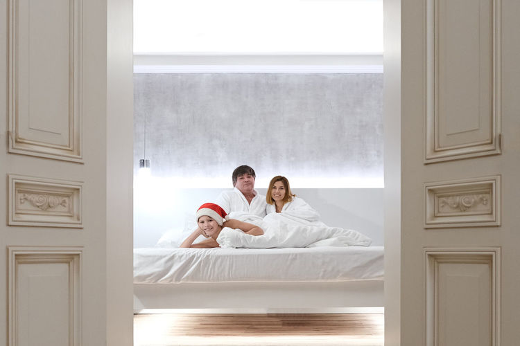 Family lies in bed waiting for santa claus for christmas. child in santa hat.