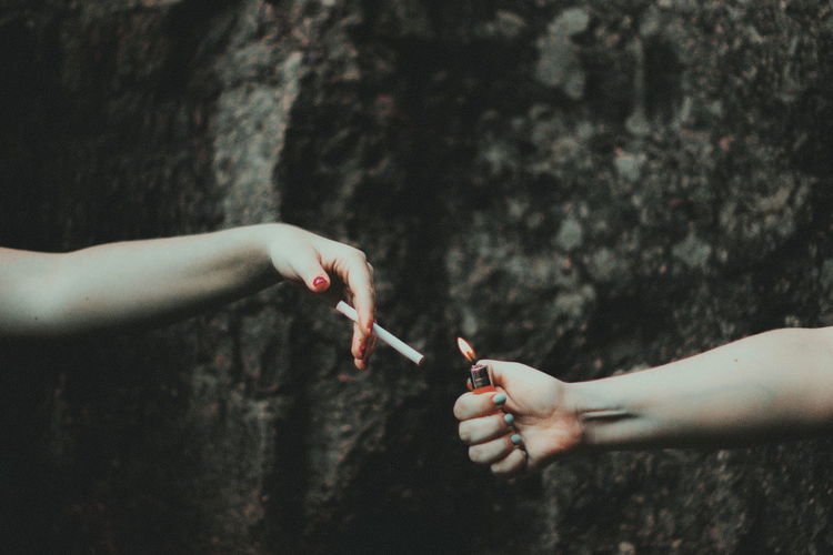 Cropped hand of woman igniting cigarette for female friend