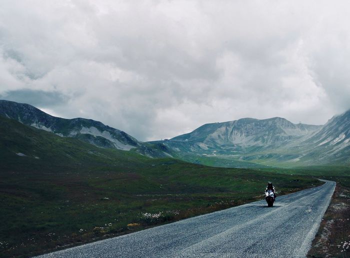 People riding motorcycle on road against mountain range