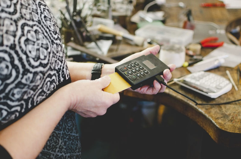 Midsection of senior woman using credit card reader in jewelry workshop