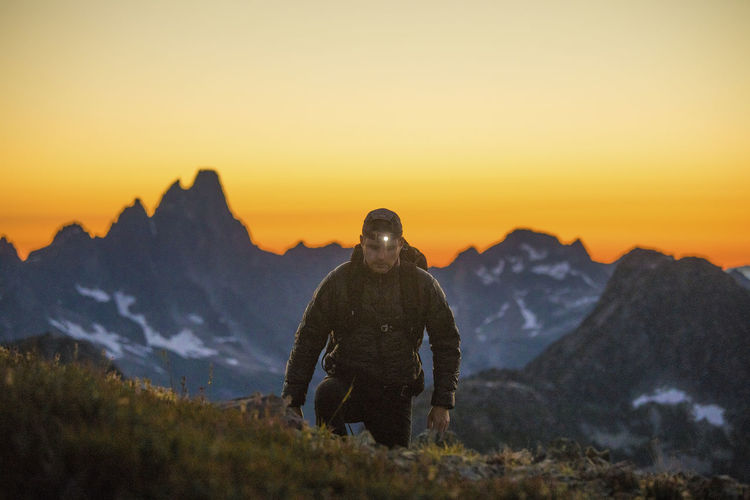 Hiker ascends mountain using headlamp after sunset.