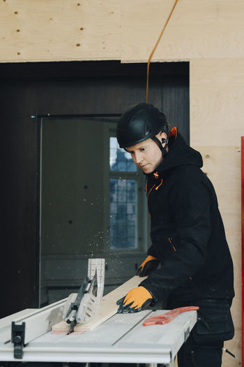 Male worker using table saw for cutting wooden plank while working at construction site