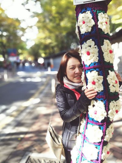 Portrait of young woman holding yarn bombing tree trunk at park