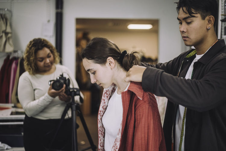 Male designer adjusting shirt collar near female model during photo shoot in studio