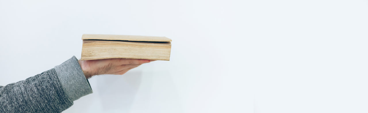 Close-up of hand holding book against white background