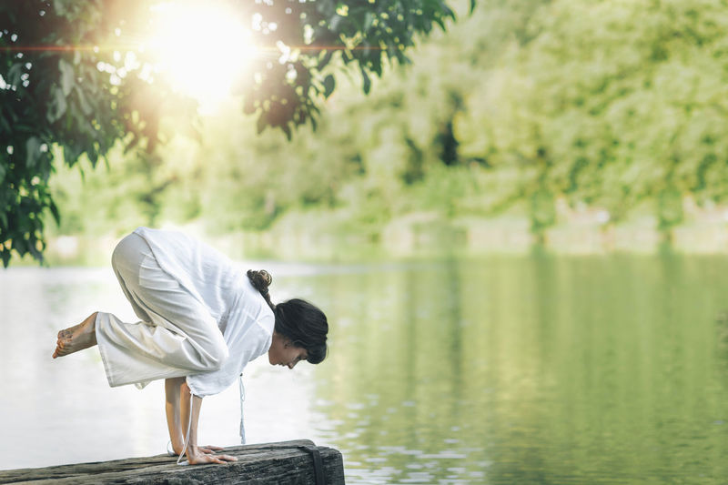 Balance and yoga. young woman doing yoga by the lake, practicing balance on hands or crow pose
