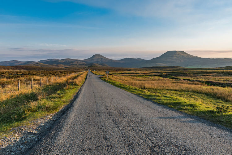 Empty road amidst field against sky