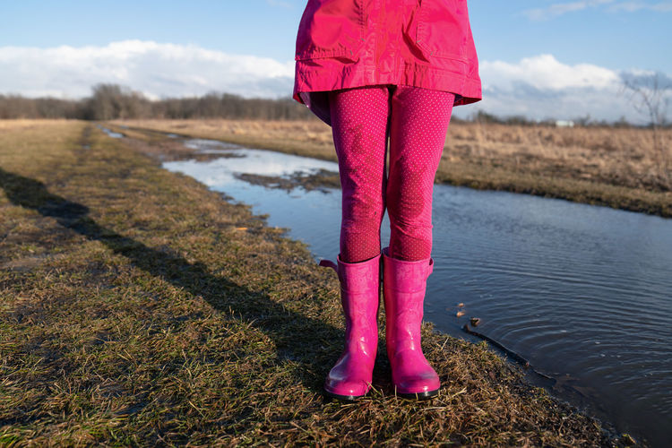 Young girl wearing pink wellie rainboots standing near a muddle puddle in spring 