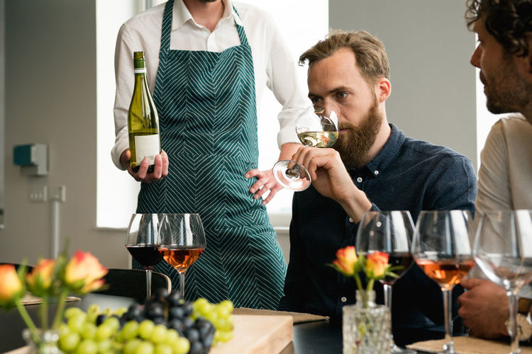 Midsection of bartender standing by customers tasting wine