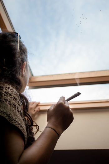 Midsection of woman holding cigarette against sky