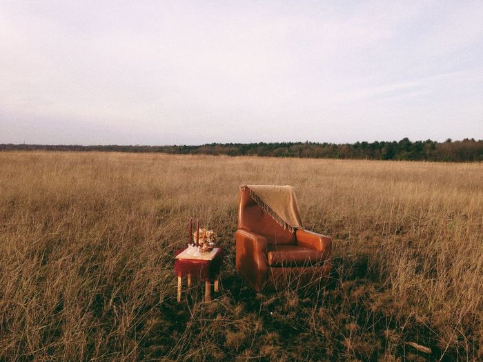 Empty chair with table on grassy field against sky