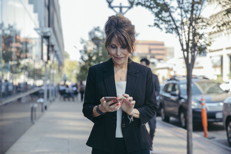 Businesswoman using smart phone on footpath