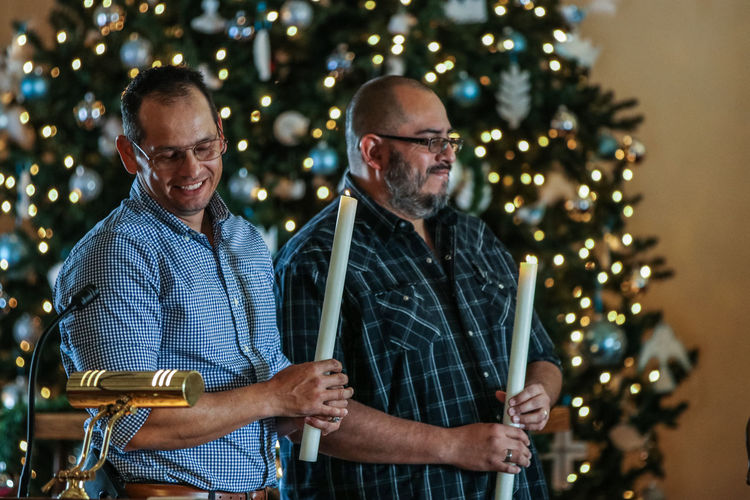 Men holding lit candles by christmas tree