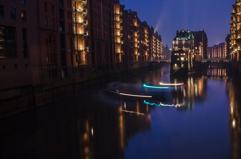Canal amidst buildings at speicherstadt during night