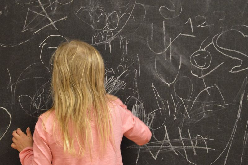 Rear view of girl writing on blackboard in school