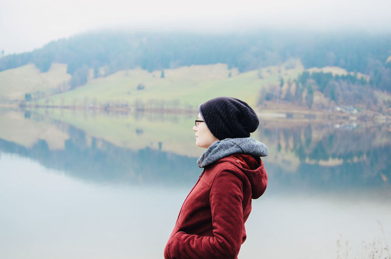 Woman looking away standing against lake during winter