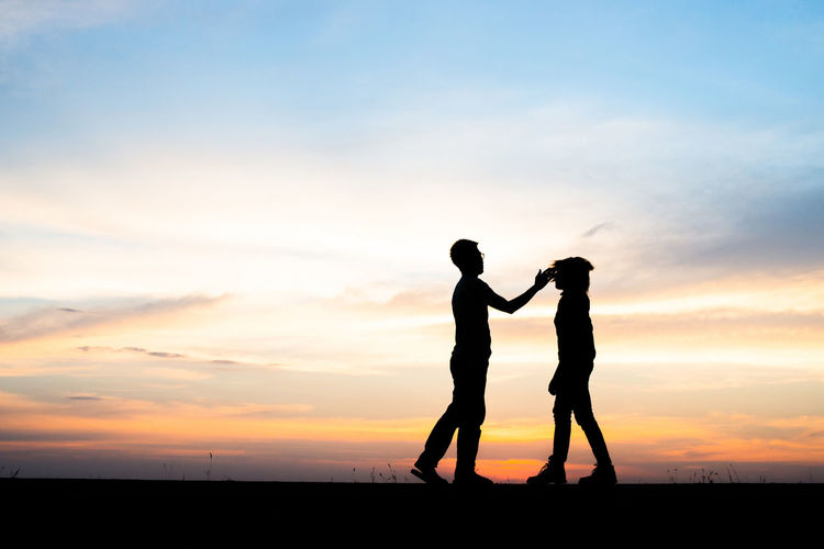 Silhouette man slapping woman against sky during sunset