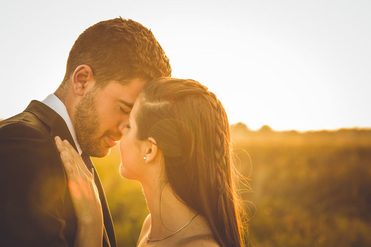 Side view of young couple kissing against sky during sunset