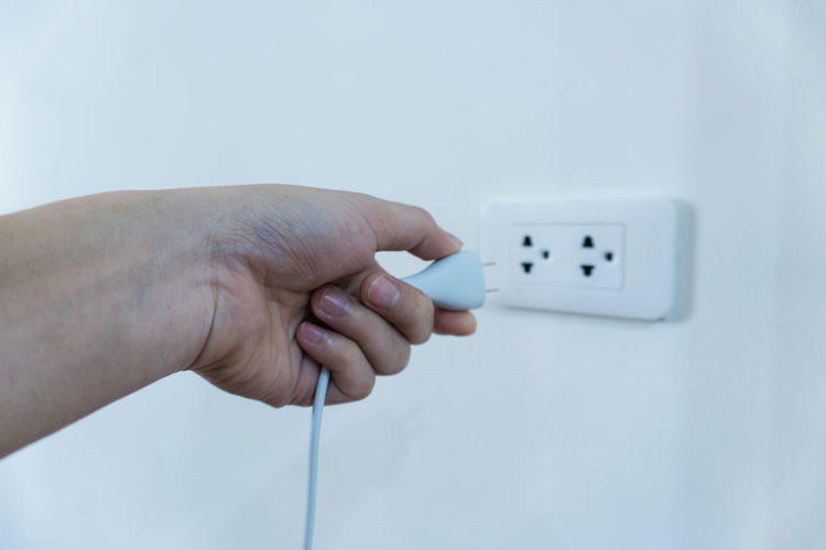 Cropped hand of woman plugging plug on wall at home