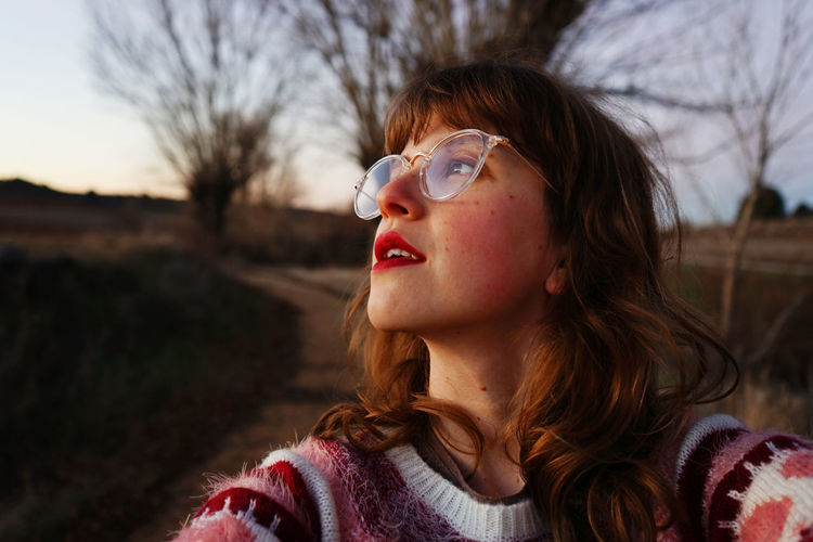 Close-up of young woman wearing eyeglasses against bare trees