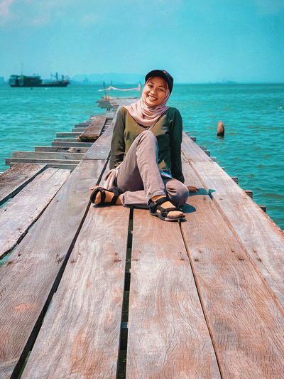 Full length of young man sitting on wood against sea