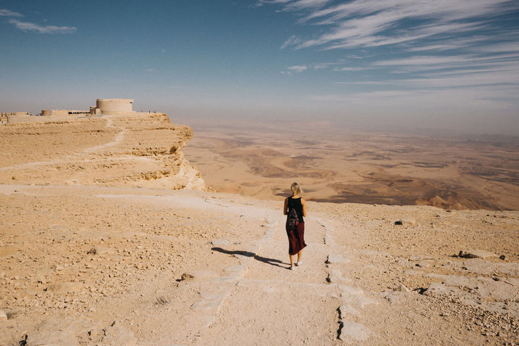 Rear view of woman walking on sand in desert against sky