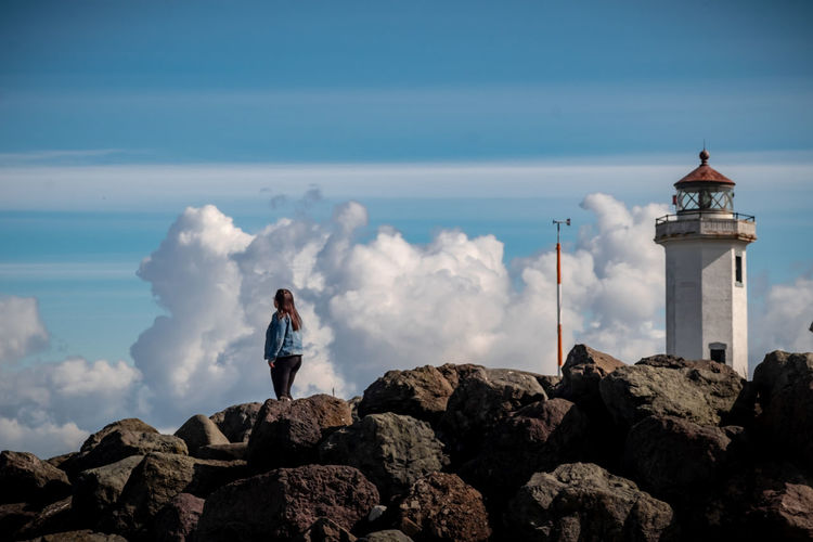 Teenage girl standing on rock by lighthouse against sky