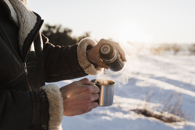 Man pouring hot coffee in cup through thermos on sunny day