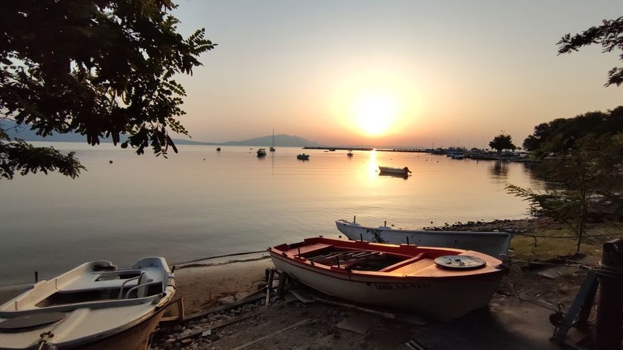 Boats moored in lake against sky during sunset