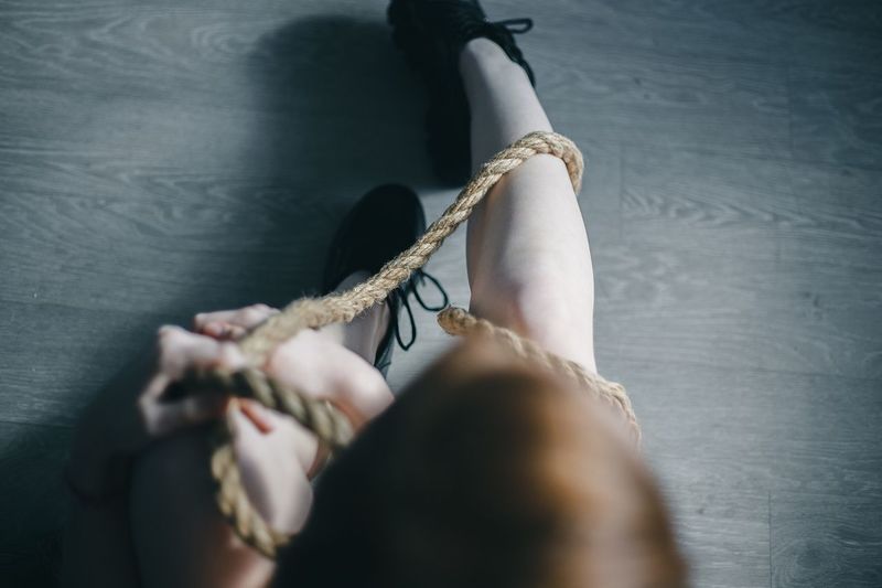 Low section of woman tied up with rope sitting on floor