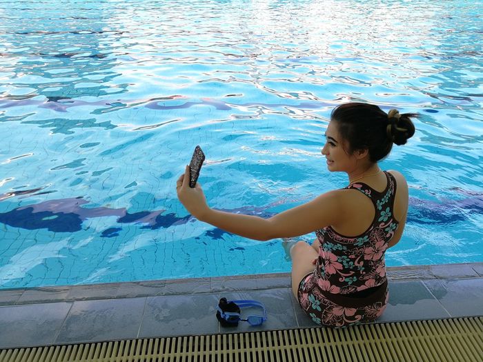 Young woman taking selfie while sitting at poolside