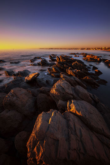 Scenic view of rocks on shore against sky during sunset
