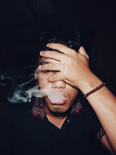 Close-up of young man smoking against black background